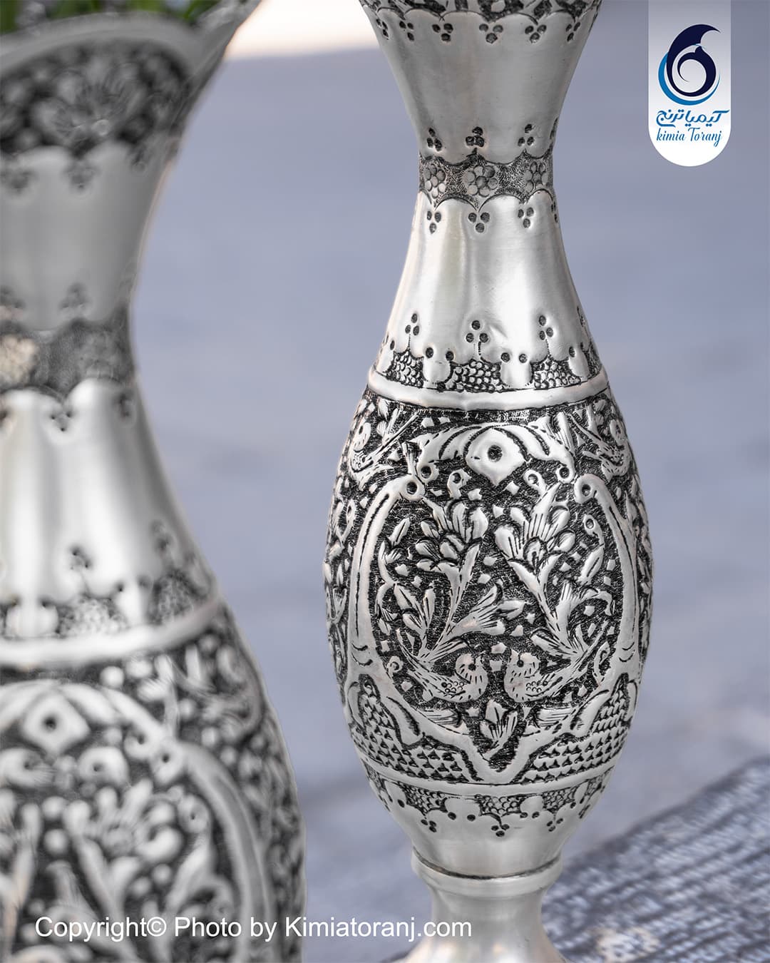 نمای نزدیک نقوش گل و مرغ قلم‌زنی‌شده روی بدنه گلدان موشکی
